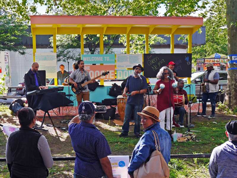 Band playing outdoors in front of brightly colored shelter structure.
Photo of "Yes Loitering" street sign in foreground with urban street scene behind.
Aerial view of walk-able strip next to road that has been painted with waves of colors.
