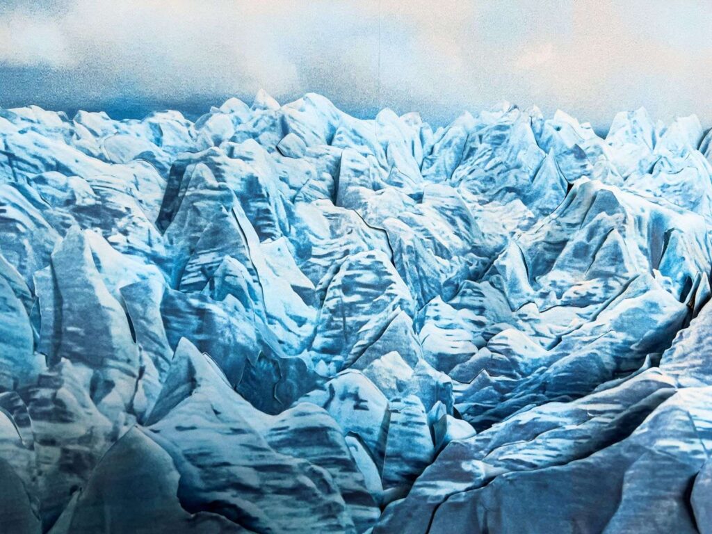 Painting of rugged blue shadowed mountain caps with foggy bluish sky in background.