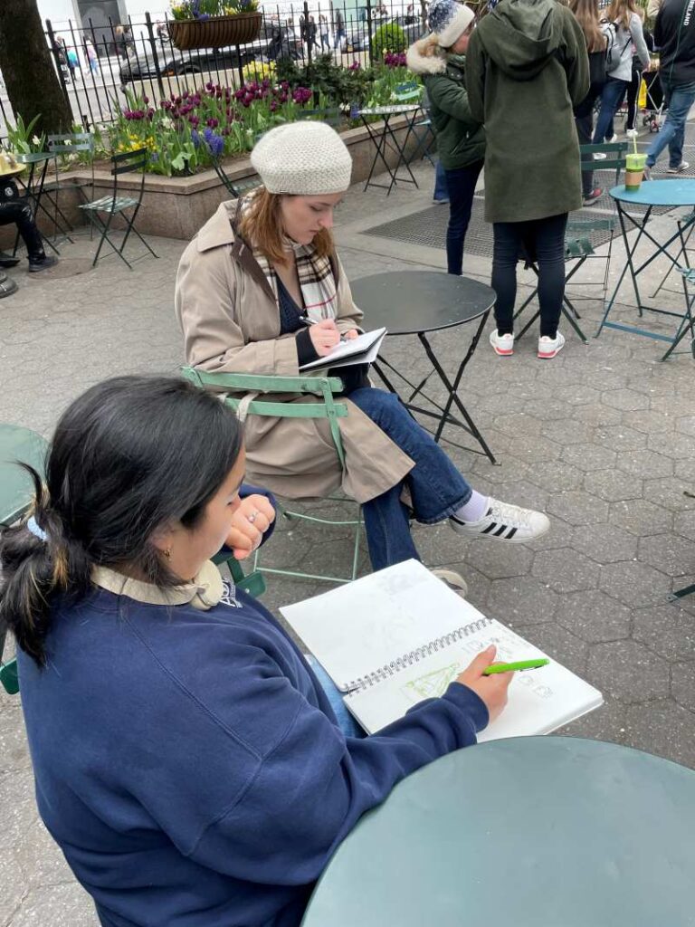 Two students sitting sketching in a park.